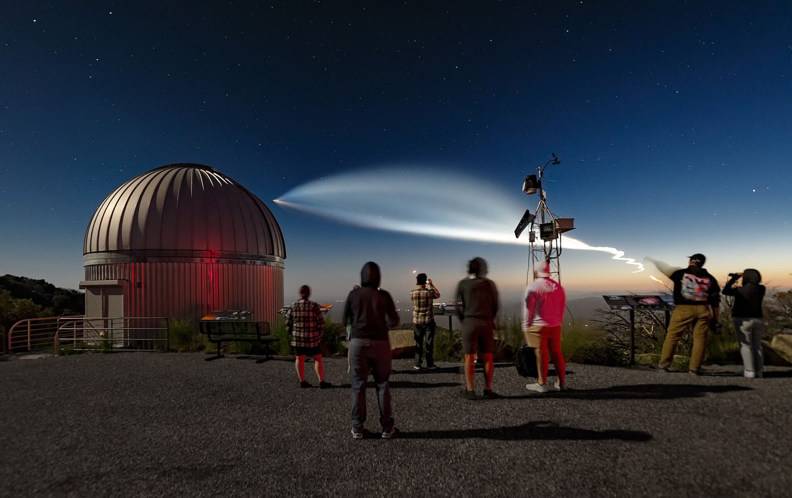 Trag lansiranja rakete Falcon 9 svijetli na sumračnom nebu iznad zvjezdarnice Kitt Peak dok ga posjetitelji promatraju
